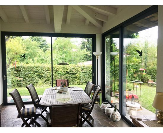 Bīdāmās ārdurvis izveidotas no alumīnija profiliem un stikla paketēm ar skatu no telpas iekšpuses uz zaļu ainavu Bīdāmās ārdurvis izveidotas no alumīnija profiliem un stikla paketēm ar skatu no telpas iekšpuses uz zaļu ainavu