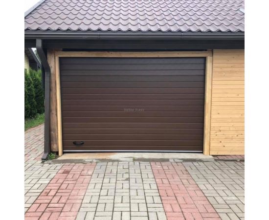 Tumši brūni sekciju garāžu vārti ar horizontālu reljefu bruģētā pagalma priekšā.